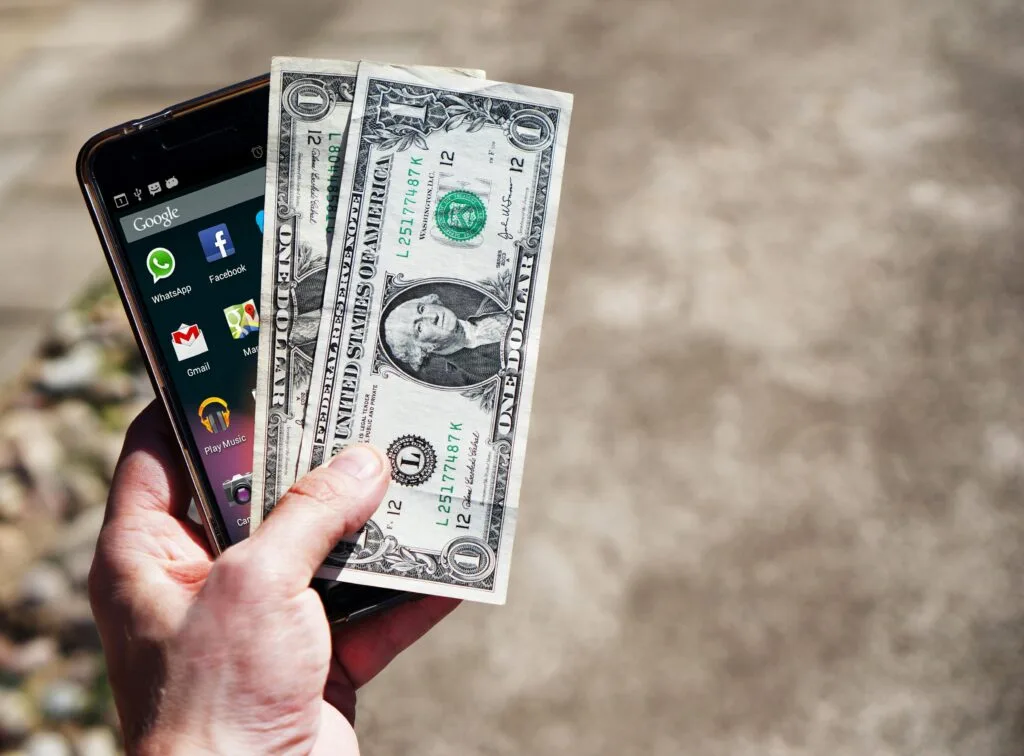 dolarové bankovky a iphone držený v ruce
