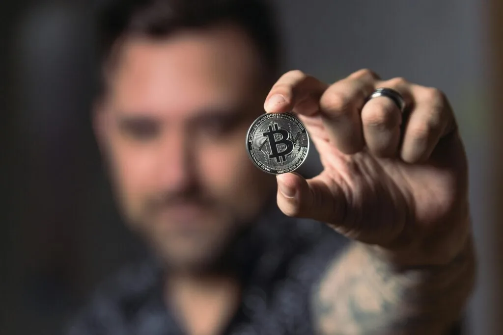 Muž držící bitcoinovou minci ve dvou prstech